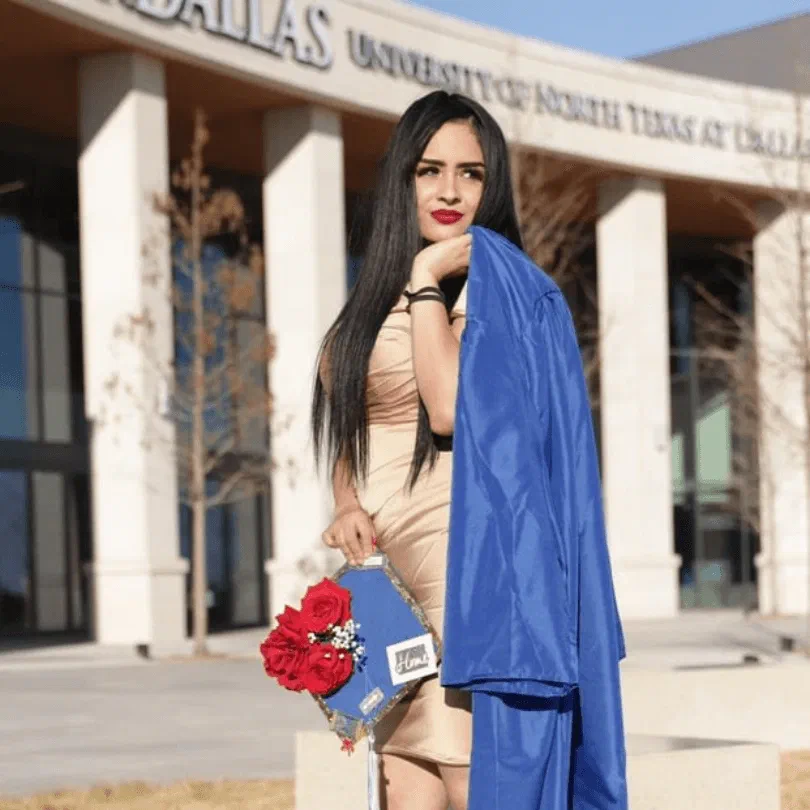 Una estudiante de Monarccast con su toga de graduación frente a la Universidad del Norte de Texas en Dallas